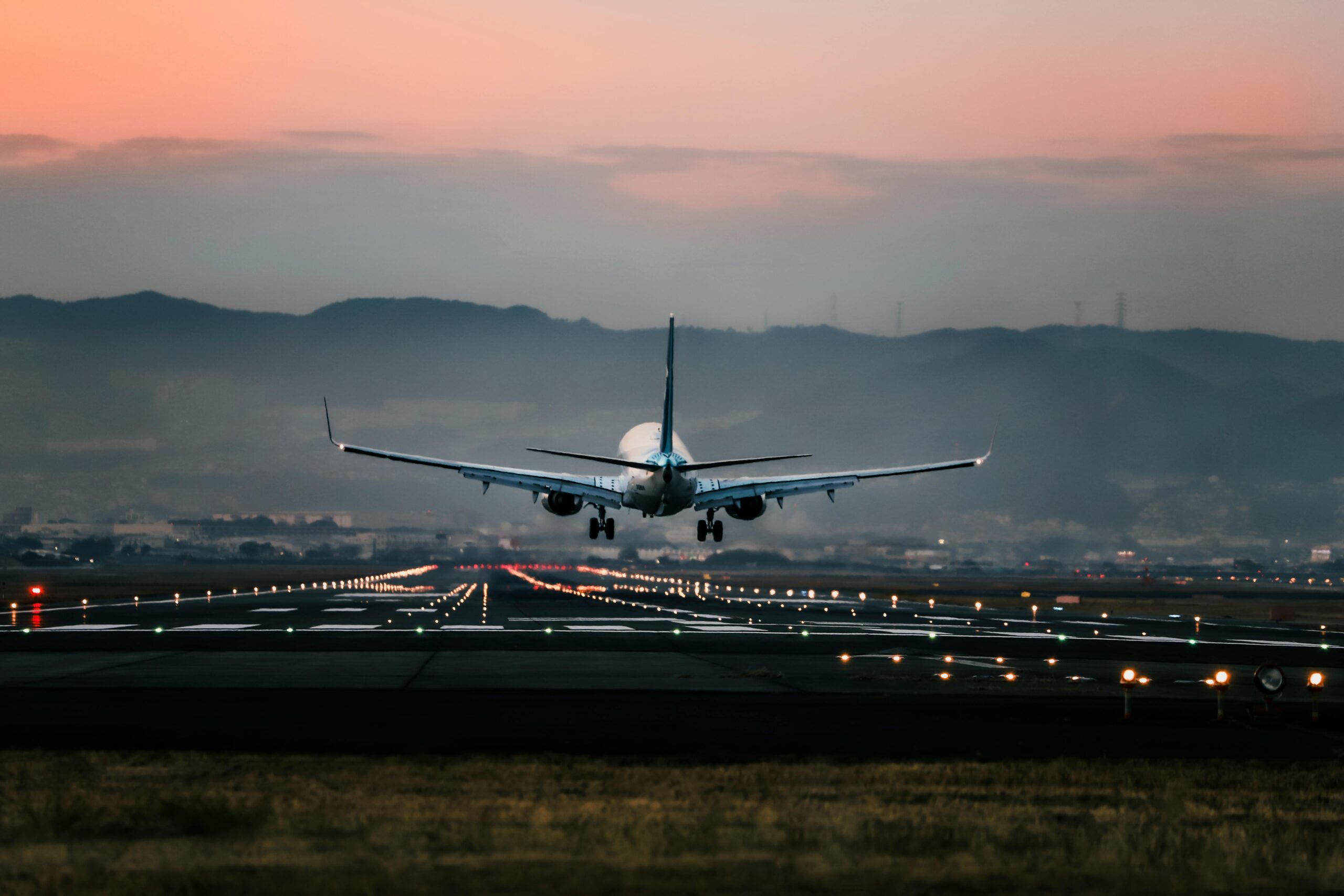 Dramatic view of a commercial airplane landing on a runway at sunset with mountains in the background.
